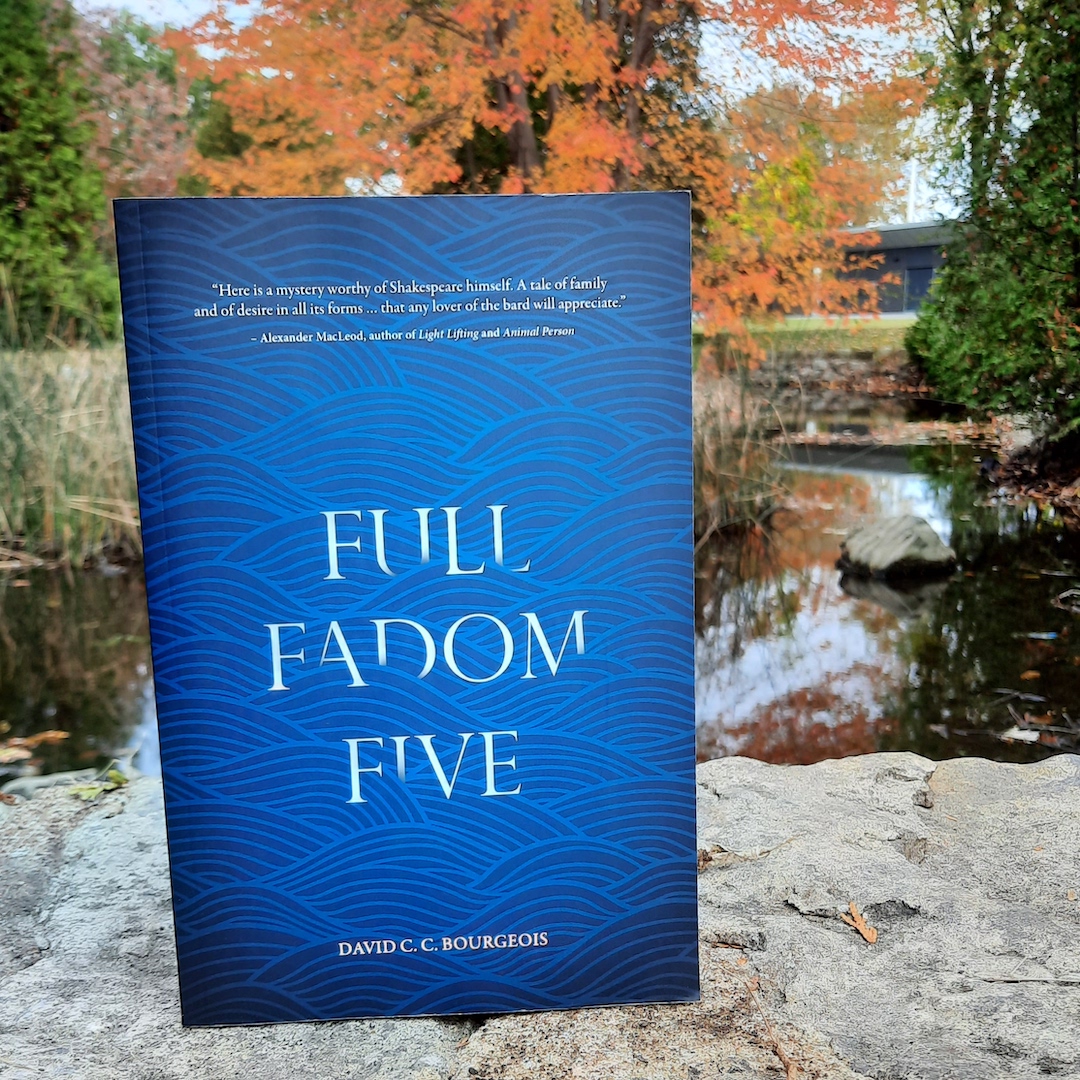 A copy of the book Full Fadom Five by David Bourgeois stands on a stone wall, overlooking a calm river and a vibrant tree in autumn.