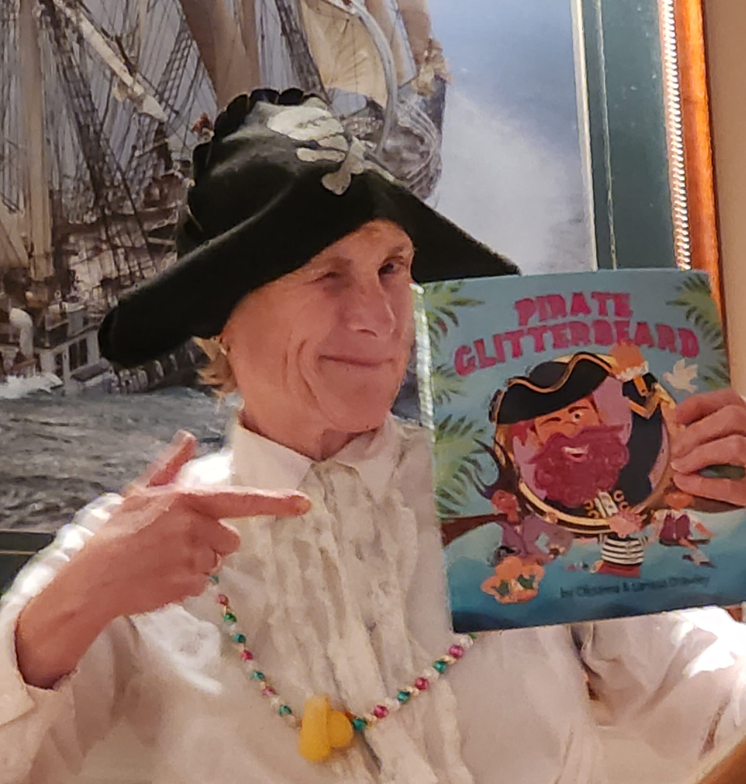 RMP Associate Publisher Cheryl Ann wears a pirate hat and points to a copy of Pirate Glitterbeard.