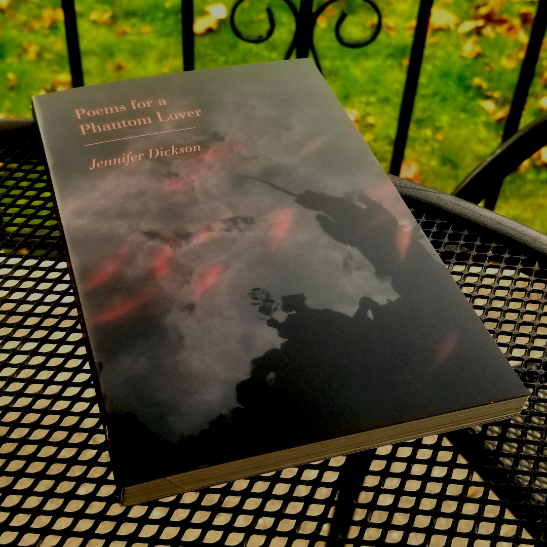 A copy of Poems for a Phantom Lover by Jennifer Dickson lays on a wire tabletop, outdoors.