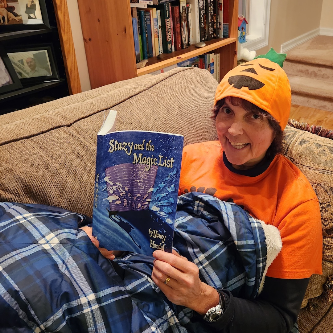 A photo of RMP publisher Lori in a pumpkin hat reading Stazy and the Magic List on the couch.