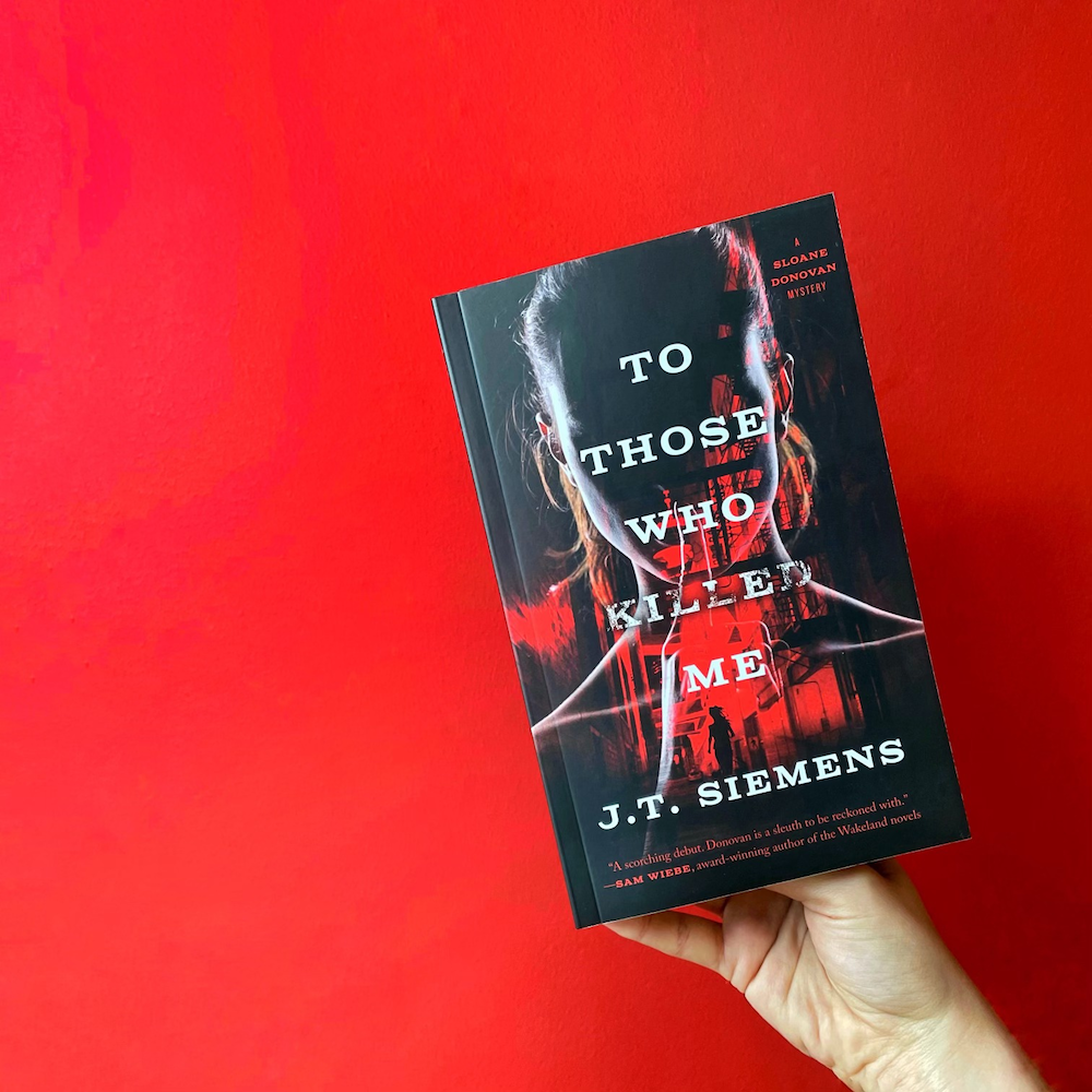 A photo of a hand holding up a copy of To Those Who Killed Me.