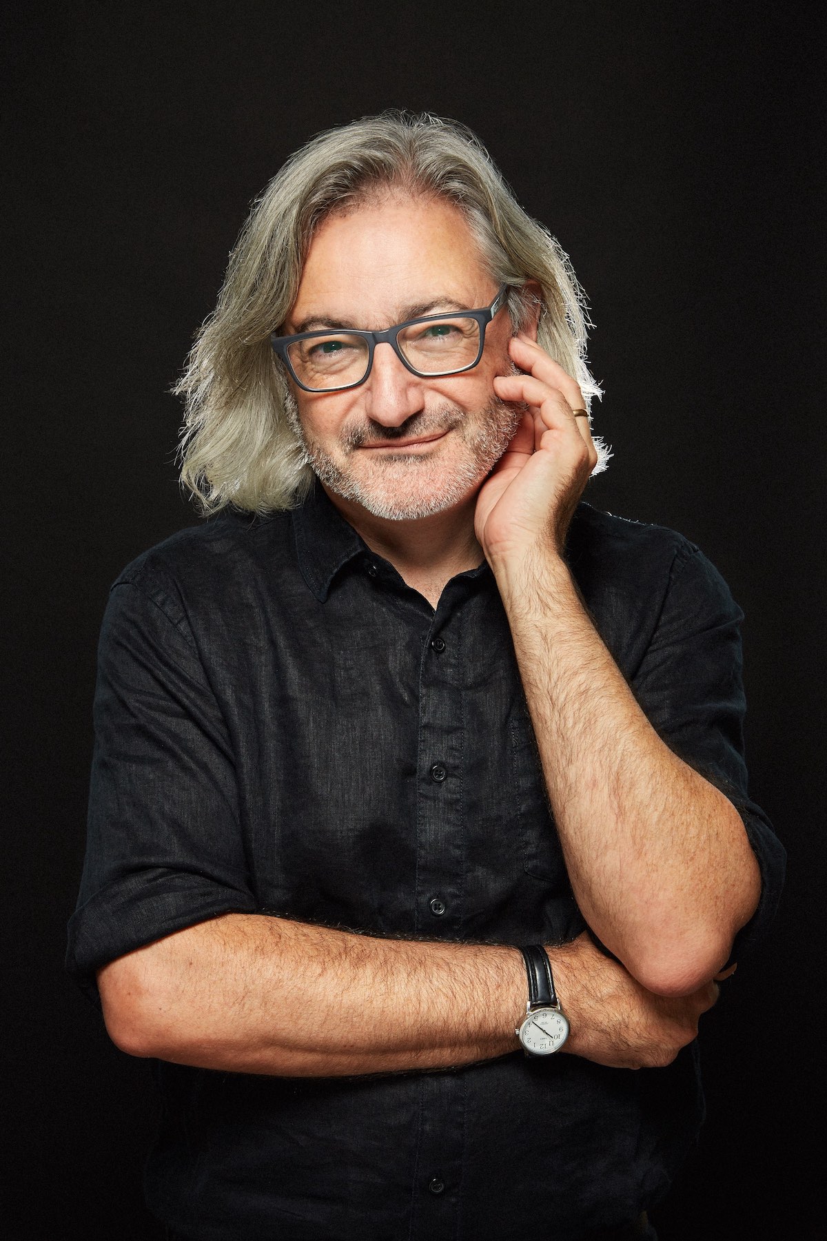 A photo of writer Gary Barwin. He is a light skin-toned man with chin-length grey hair and glasses, and he wears a black button down shirt against a black background.