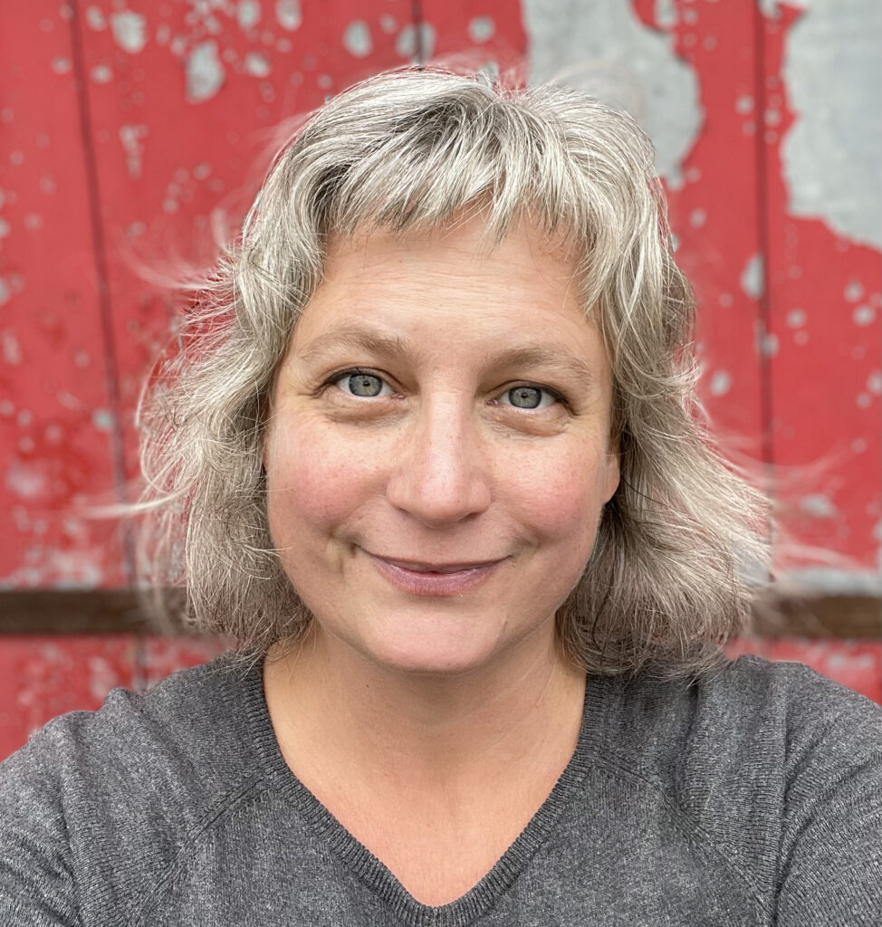Photo of author Emily Pohl-Weary, a woman with shoulder-length blond hair and blue eyes. She is wearing a grey shirt and smiling into the camera.