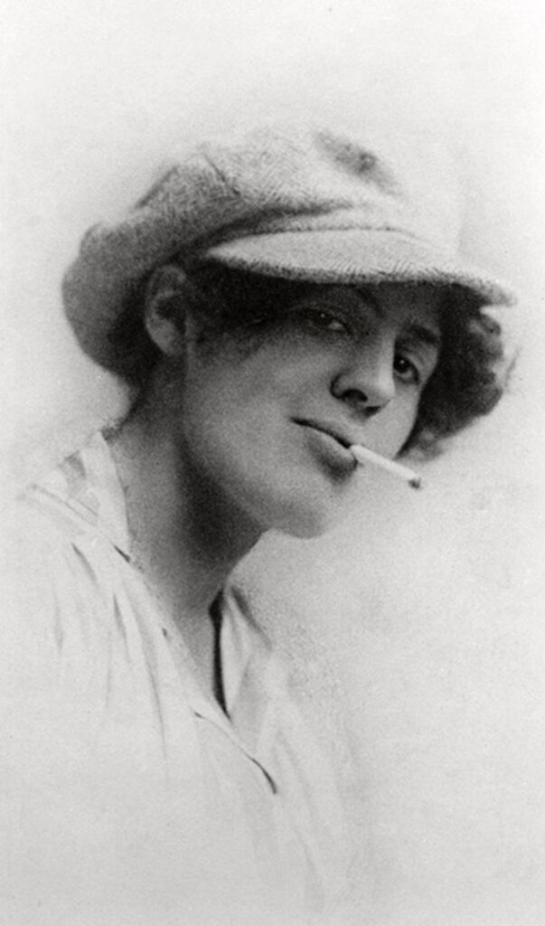 A vintage, black and white photo of Jessie, a woman with short hair under a cap, a cigarette dangling from her mouth. She looks confident and bold.