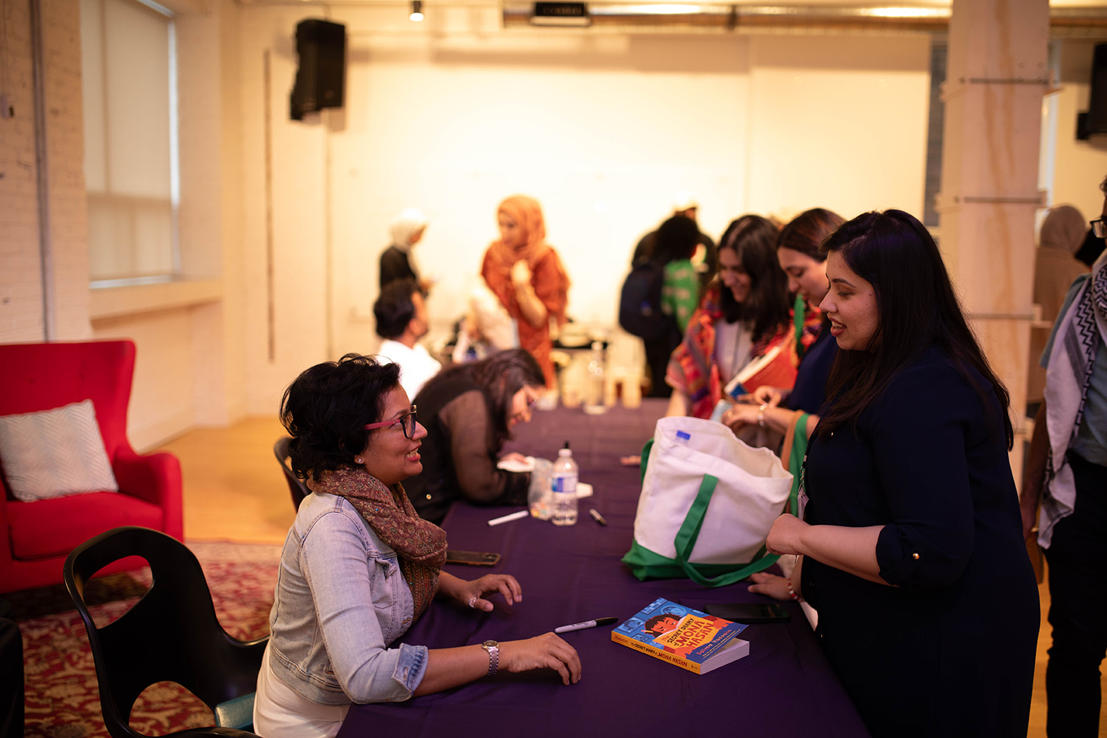 Women talking along a signing table at the Muslim Literary Festival. They are in conversation, smiling, exchanging books to be signed.