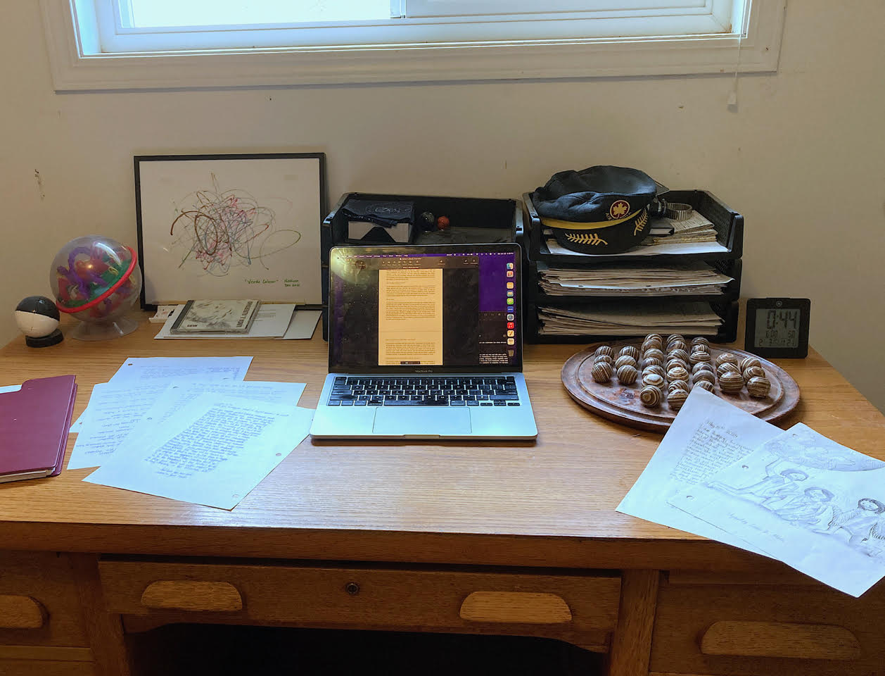 A photo of Nathan's workspace. On an antique-looking wooden desk, various orbs, a "scribble" drawing, a laptop computer, and handwritten sheets of paper and drawings are scattered around the desk. There is a wooden solitaire game on the desk as well. A timer reading 0:44 sits in the right corner.