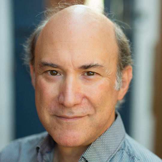 A photo of Raymond Beauchemin. He is a light skin-toned man with a bald head and grey hair, smiling slightly.