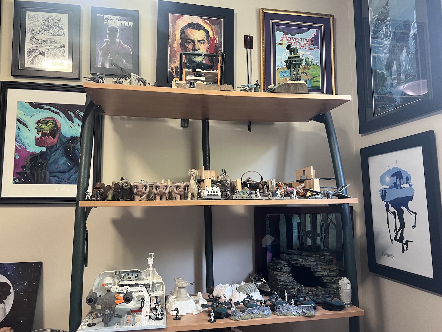 The view from Richard Van Camp's writing chair, showing three shelves filled with Star Wars figurines, the wall covered in artwork from sci-fi and fantasy.