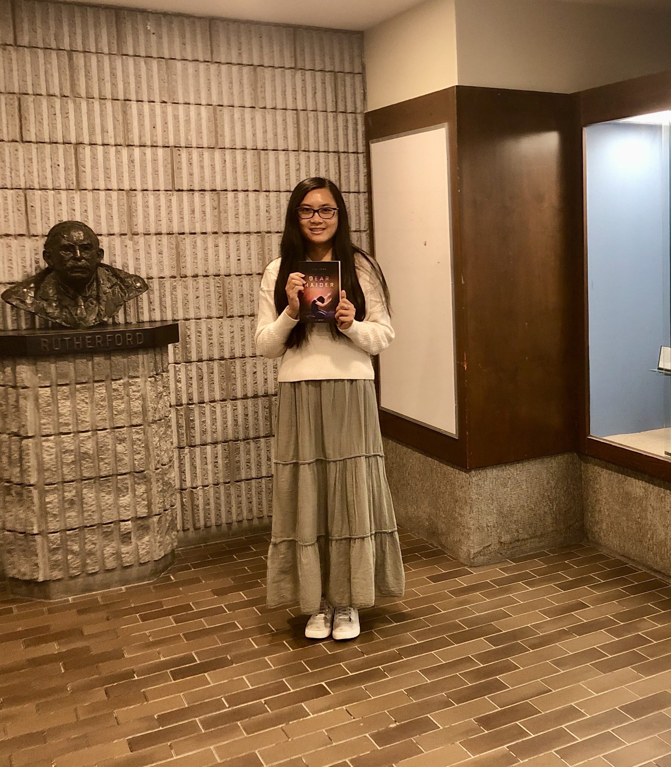 A photo of Lili Zeng with her book Dear Haider. She is standing in the lobby of the Ernest Rutherford Physics Building, which hosts the Department of Physics of McGill University.