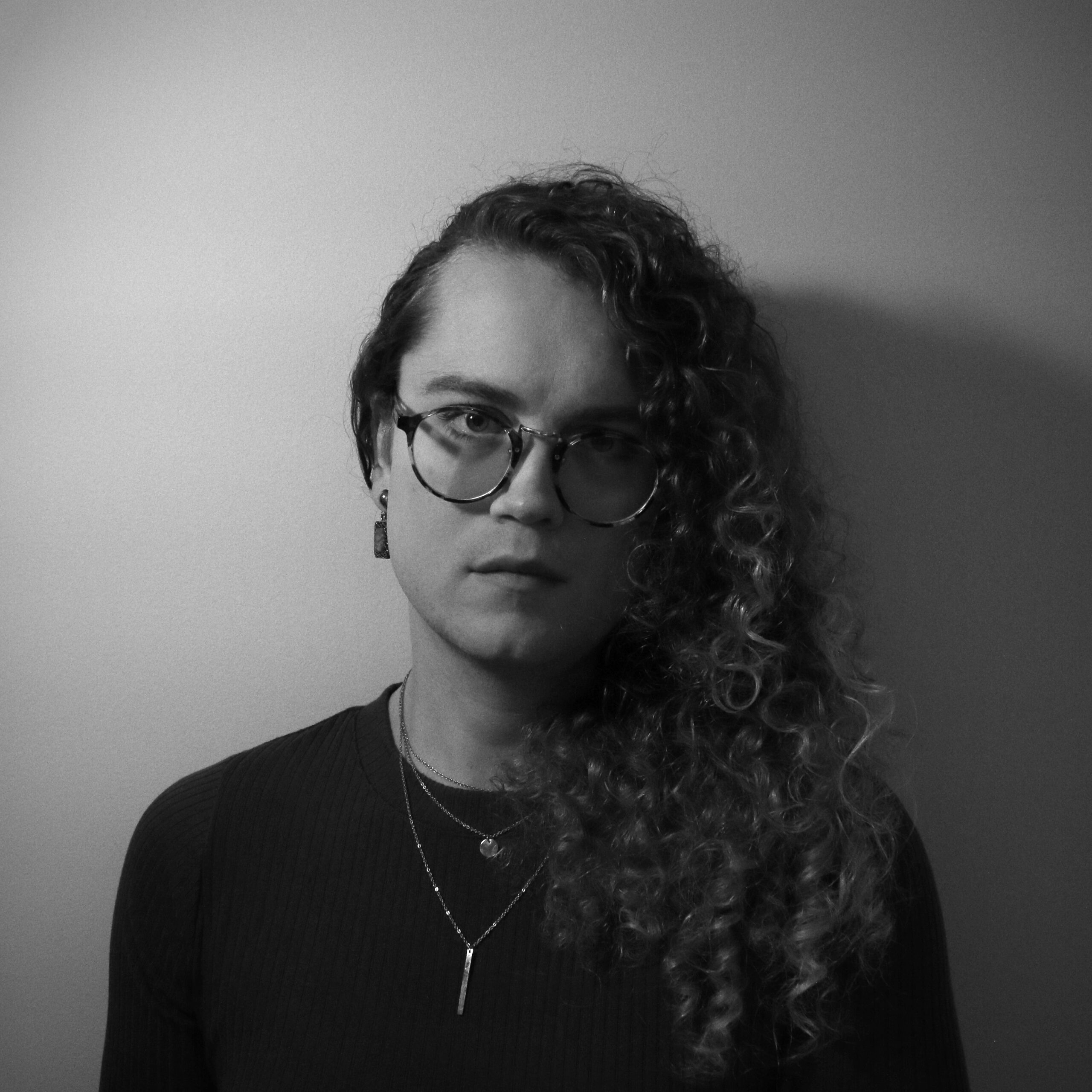 A photo of author Harman Burns, a light-skin-toned trans woman with long curly dark hair and glasses.