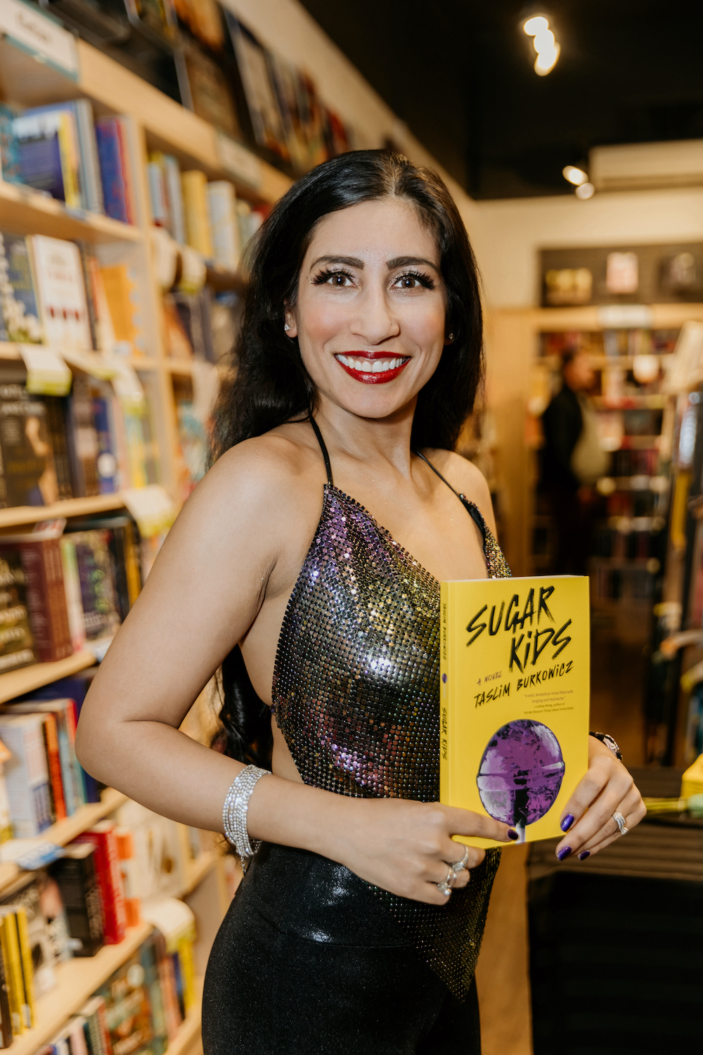 A photo of Taslim Burkowicz at her book launch, holding a copy of her book Sugar Kids.