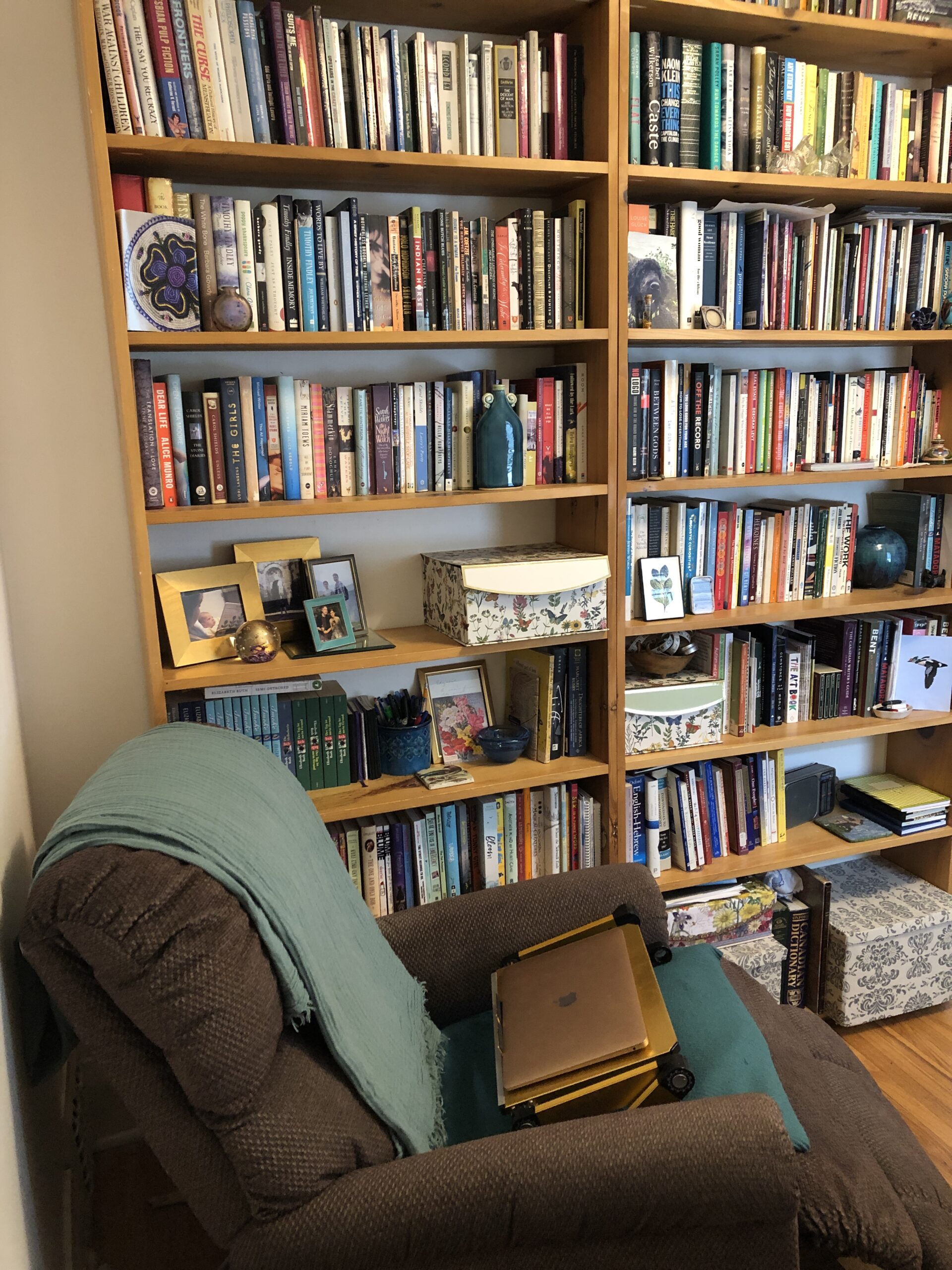 A photo of Elizabeth Ruth's writing space. There are oak bookshelves filled with books and a brown lounge chair with a laptop computer on it.