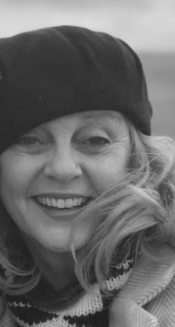 A close-up photo of writer M.V. Feehan. She is a light skin-toned woman with light-coloured hair, wearing a slouchy dark hat and beaming out at the camera.