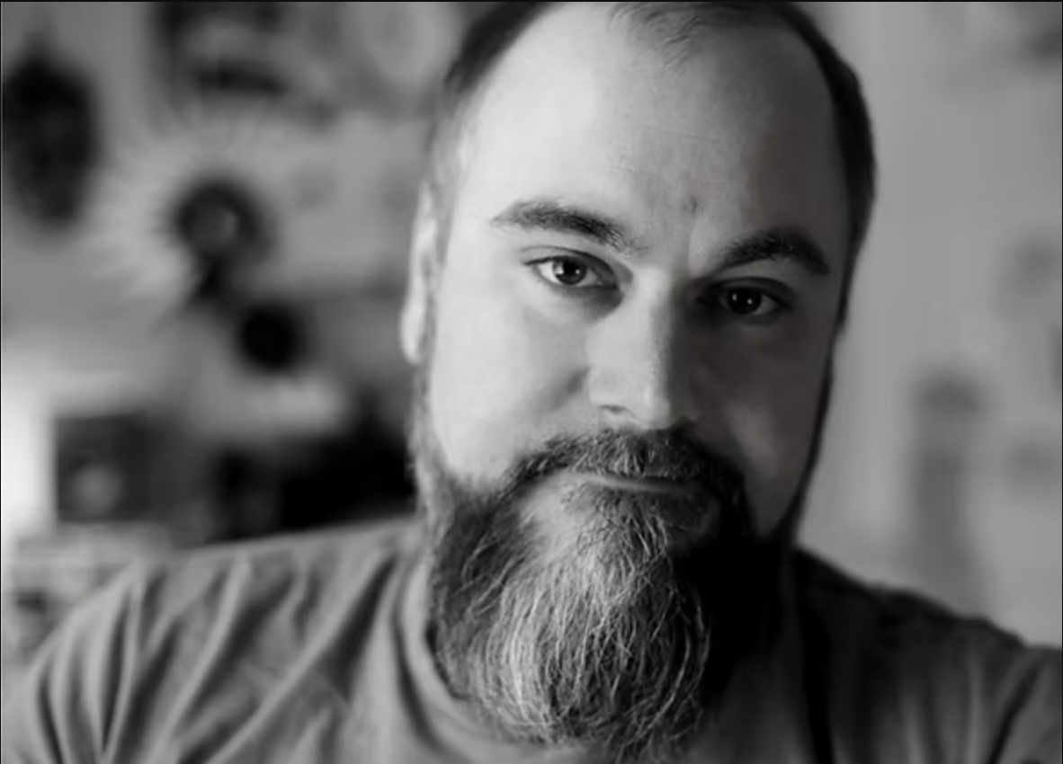 A black and white photo of writer J.R. McConvey. He is a light skin-toned man with a bushy beard.