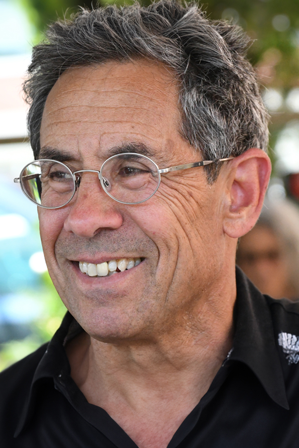A photo of Dan Yashinsky, a light-skin-toned man with short salt-and-pepper hair and round-framed glasses. He is smiling at something just out of the frame.