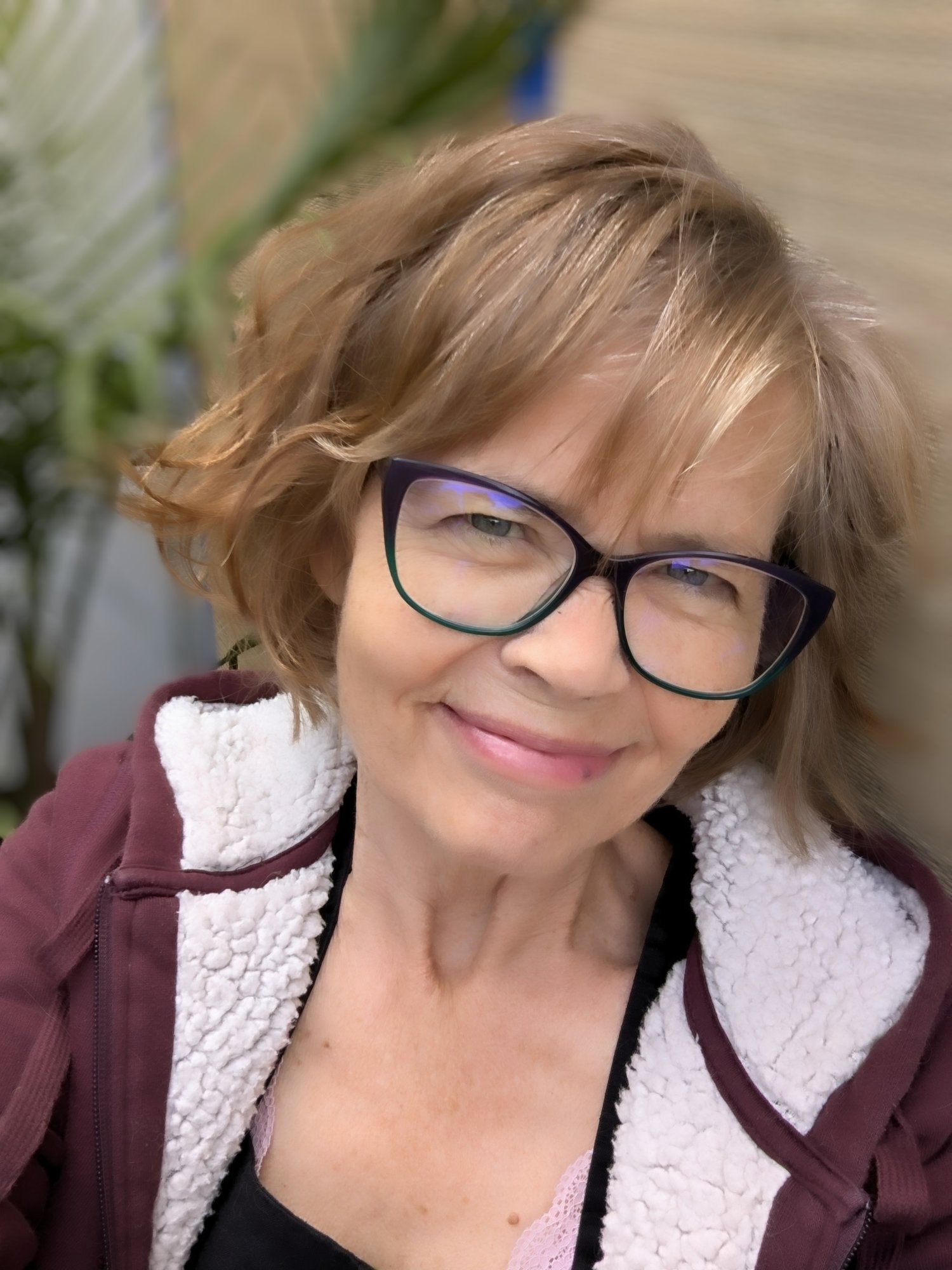 A photo of writer Anna Dowdall. She is a light skin-toned woman with short, feathered brown hair and glasses, wearing a zip hoodie.