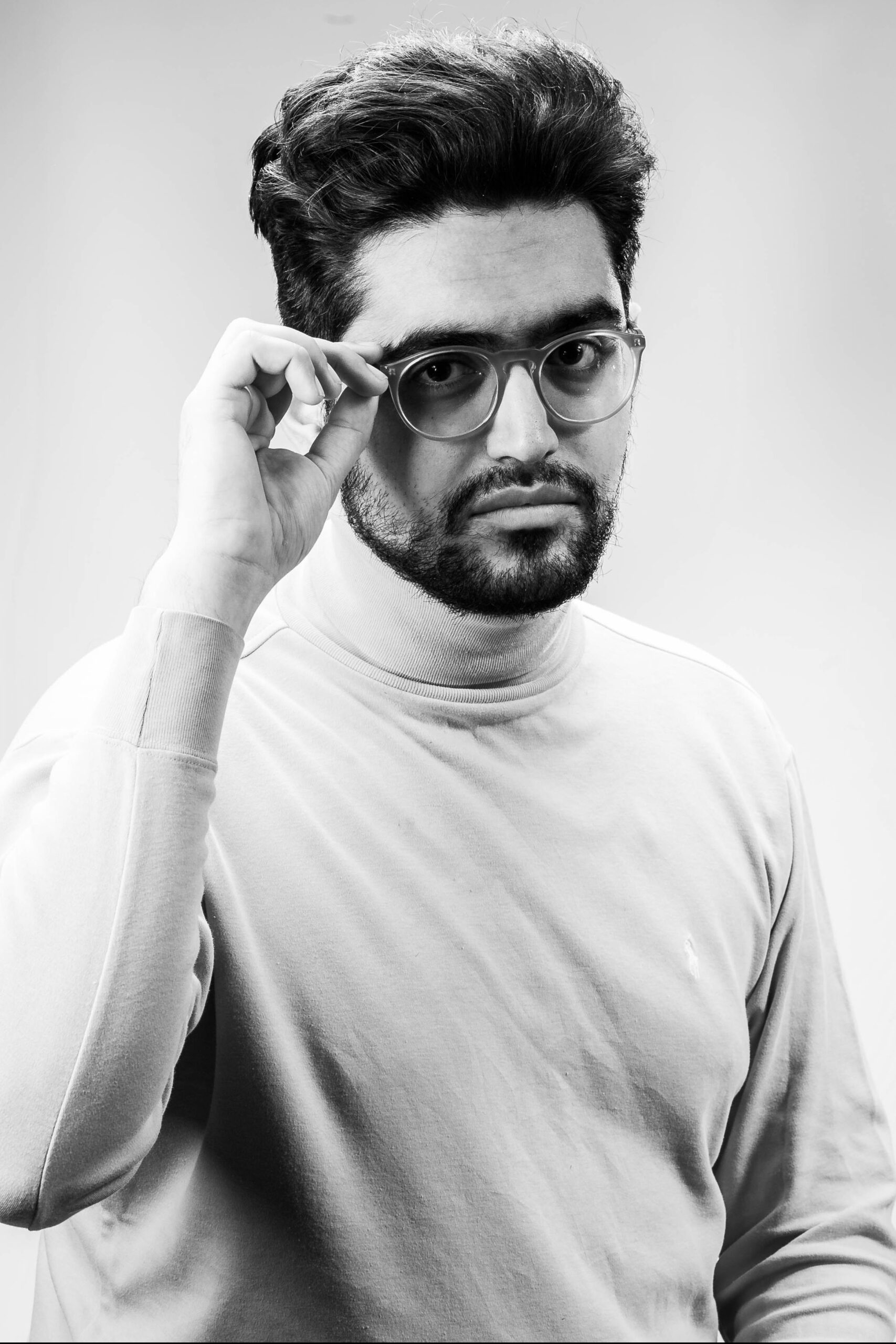 A black-and-white photo of author Khashayar “Kess” Mohammad. They have short dark hair and a short beard. They are wearing glasses and a turtleneck. 