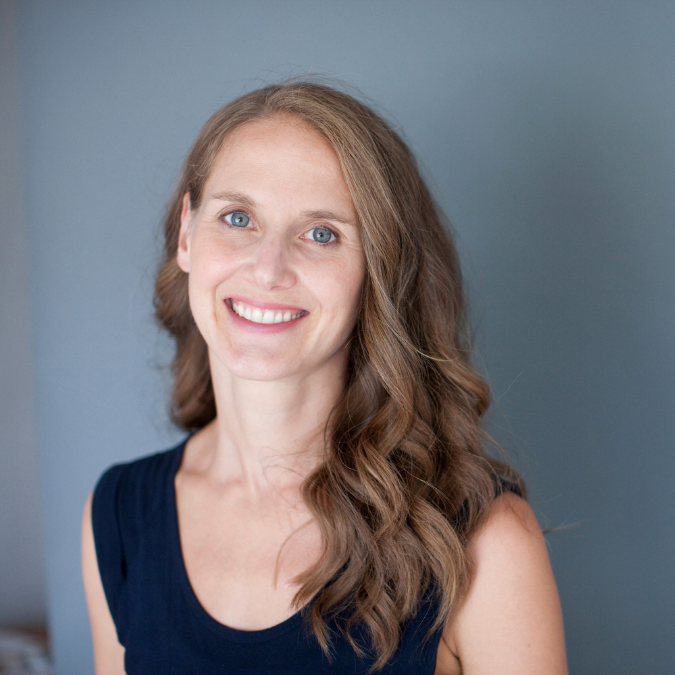 A photo of writer Linday Zier-Vogel. She is a light skin-toned woman with long, wavy light brown hair and blue eyes. She wears a sleveless navy top and smiles at the camera.