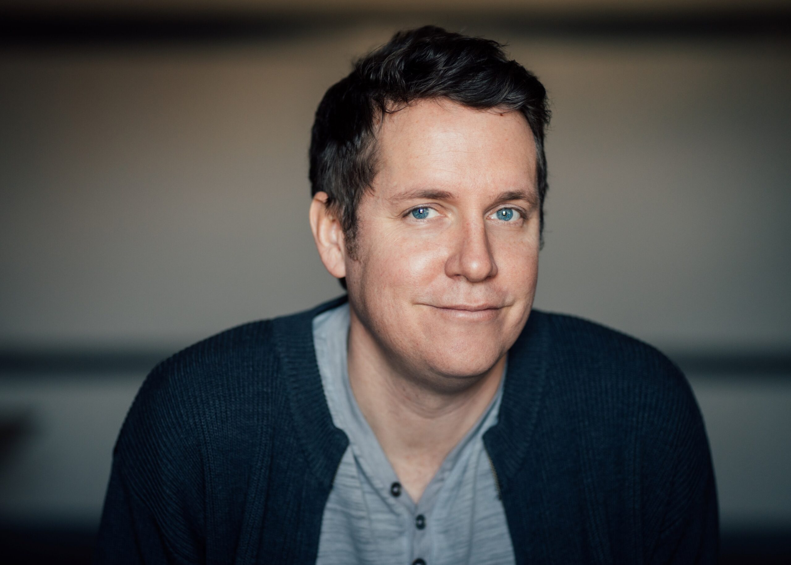 A photo of Nick Thran. He is a light-skin-toned man with short dark hair and blue eyes. He is wearing a grey shirt under a navy blue cardigan.