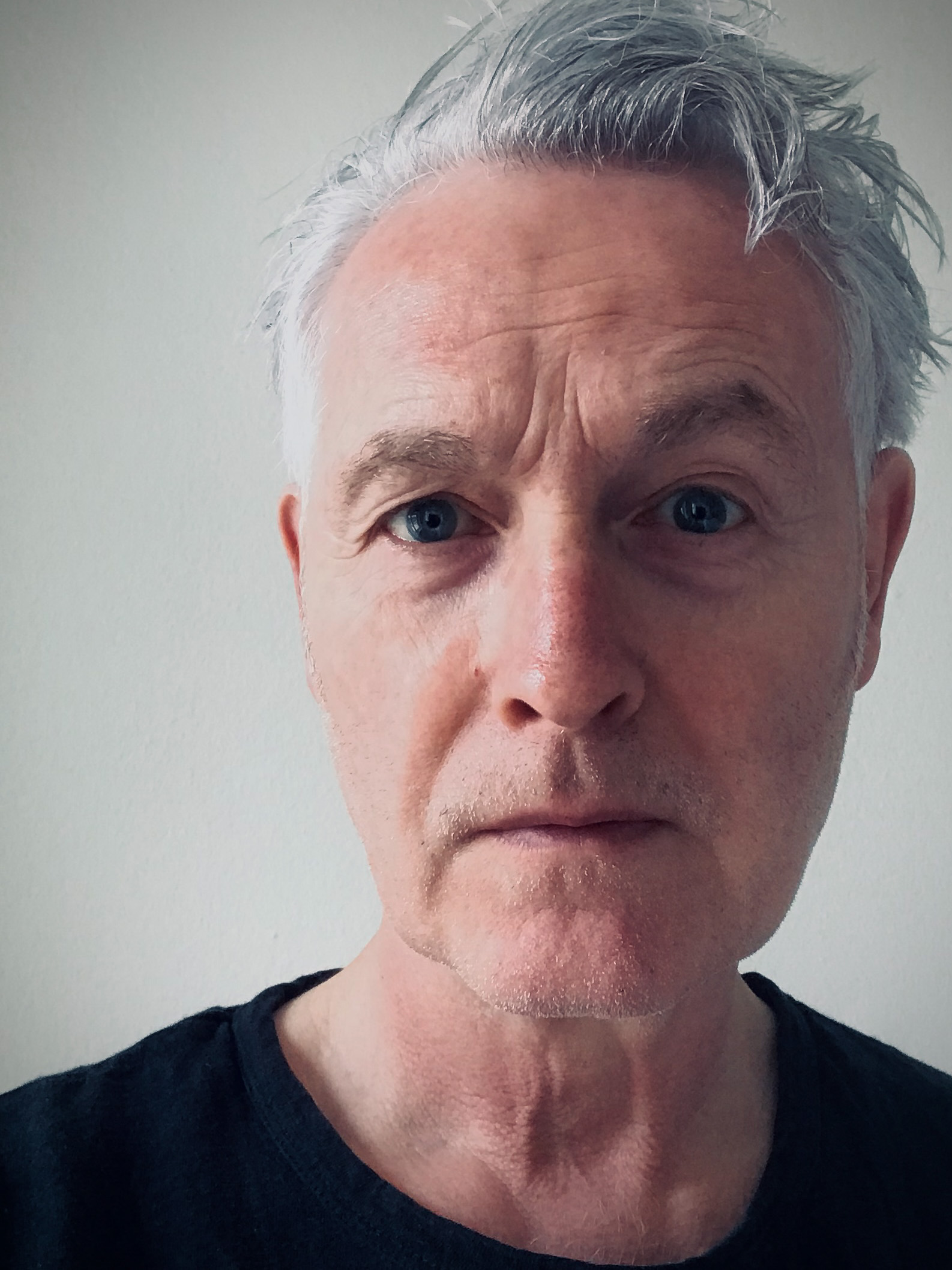 A close-up photo of Martin Aitken. He is a light-skin-toned man with short grey hair styled to the side. He is wearing a black shirt and looking into the camera.