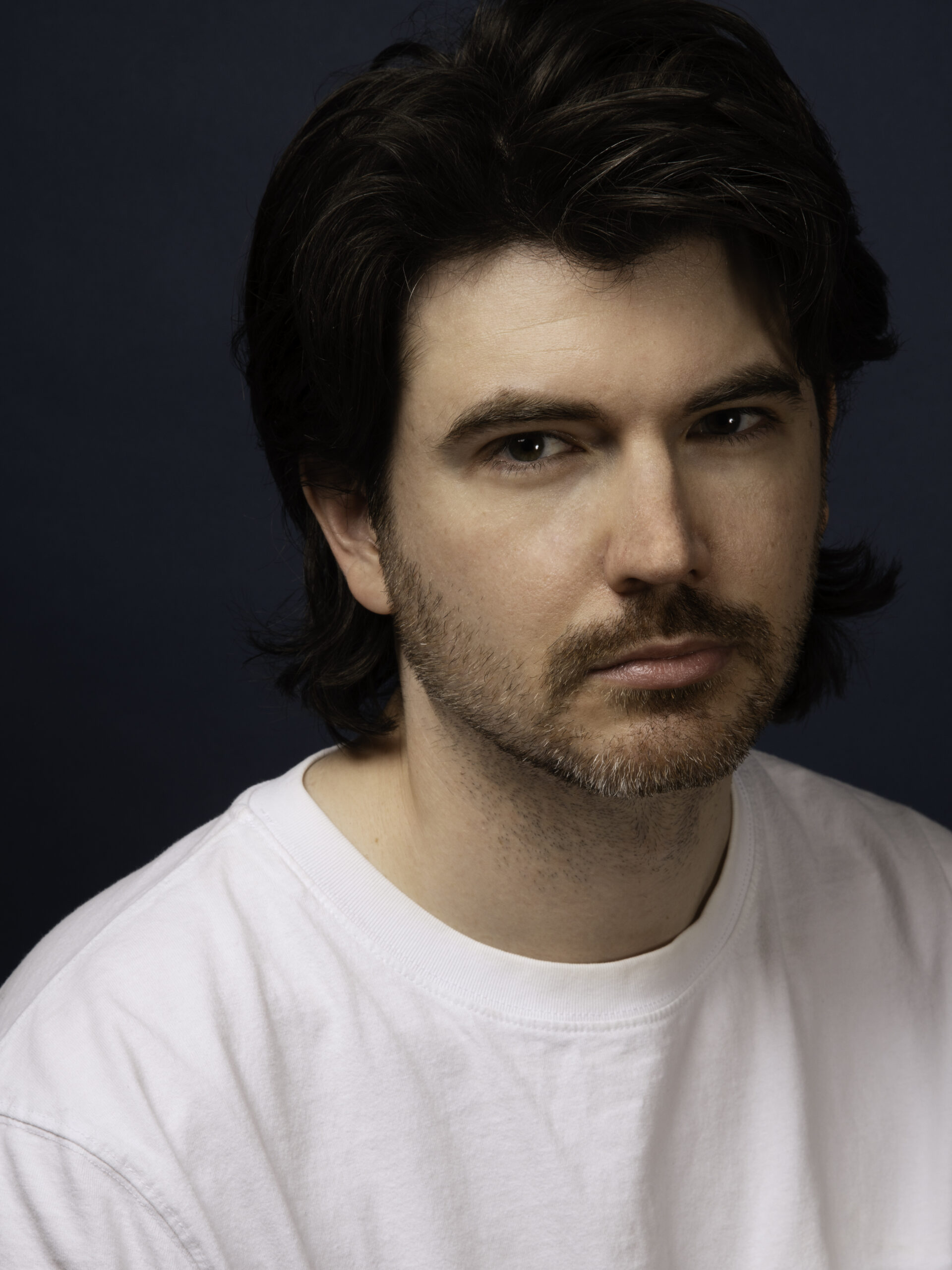 A photo of Jason Purcell. They are light-skin-toned person with dark brown hair parted to the side, brown eyes, and facial hair. They are wearing a white shirt and looking into the camera.